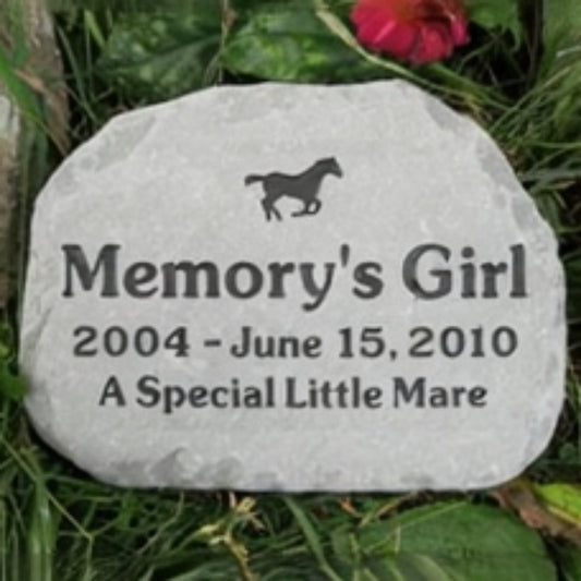A personalized horse memorial stone engraved with the name 'Memory's Girl', dates '2004 - June 15, 2010', and the phrase 'A Special Little Mare' with a small horse silhouette, placed outdoors in grass among green leaves.