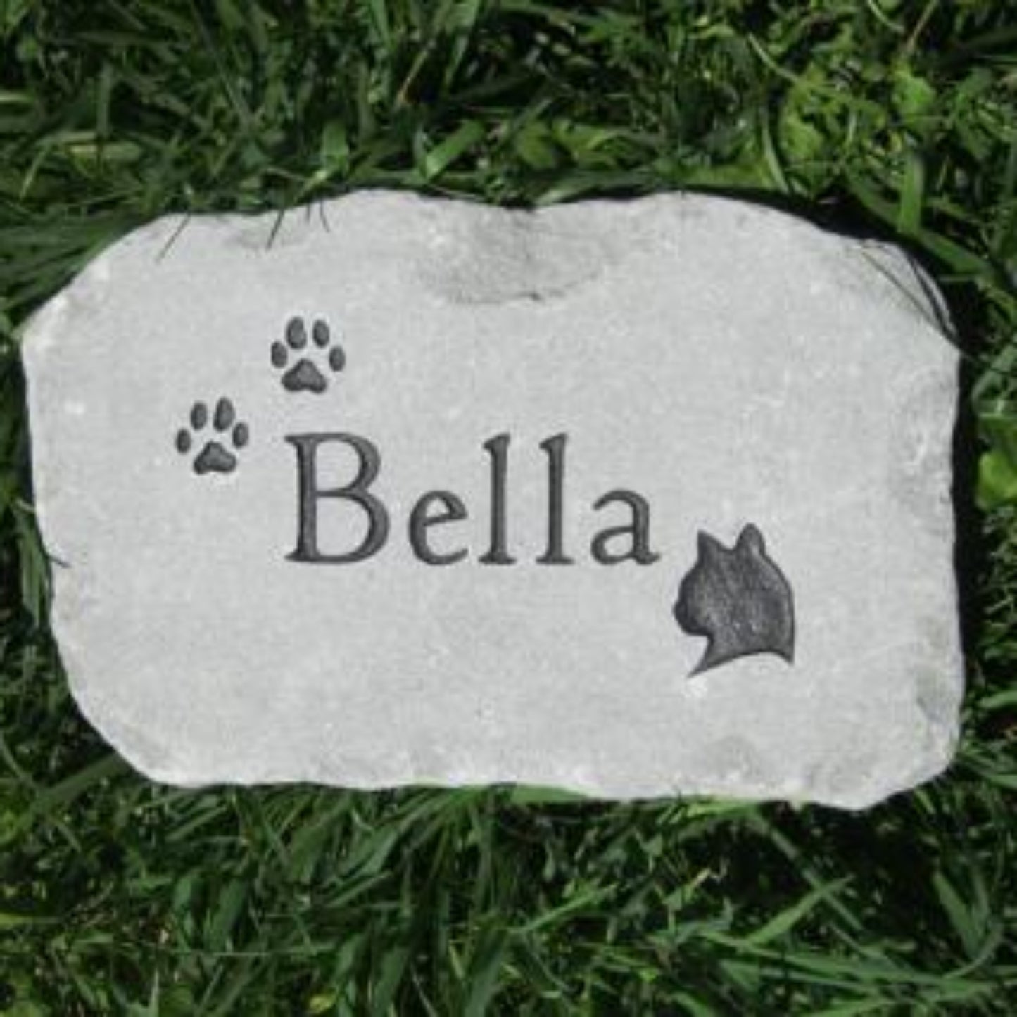 A personalized cat memorial stone engraved with the name 'Bella', paw prints, and a cat silhouette, resting on green grass.