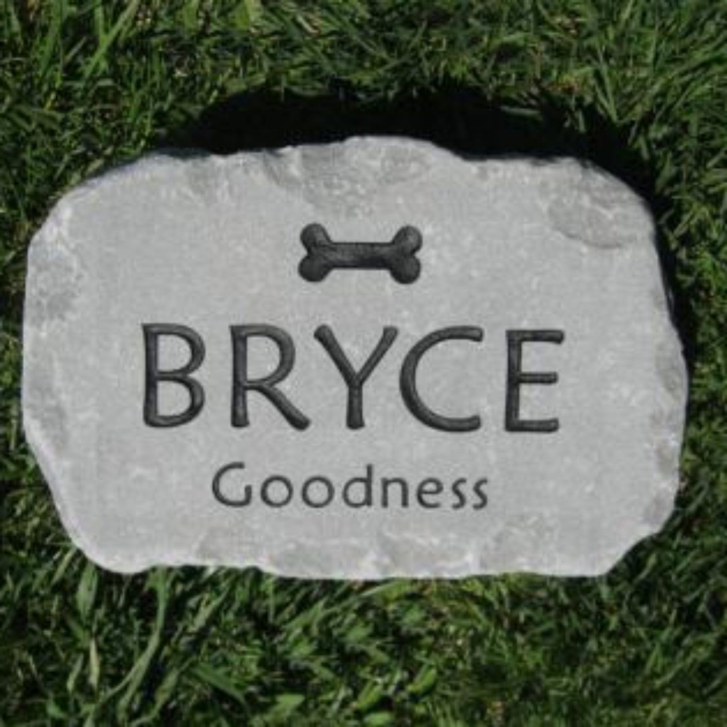 A personalized pet grave stone shaped like a natural rock, engraved with a bone icon, the name 'BRYCE', and 'Goodness' on a green grass background.