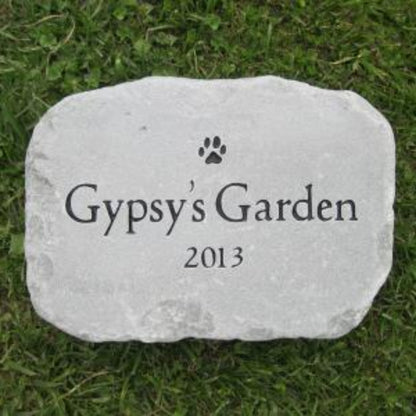 A personalized pet memorial garden stone engraved with 'Gypsy's Garden', a paw print, and the year '2013', resting on green grass.