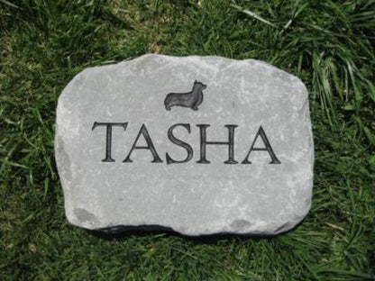 A personalized gray stone pet memorial marker engraved with the name 'TASHA' and a small dachshund silhouette, placed on green grass.