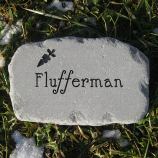 A custom engraved garden stone for a bunny featuring the name 'Flufferman' in a decorative font with a small carrot silhouette above it, placed on grass with patches of snow.