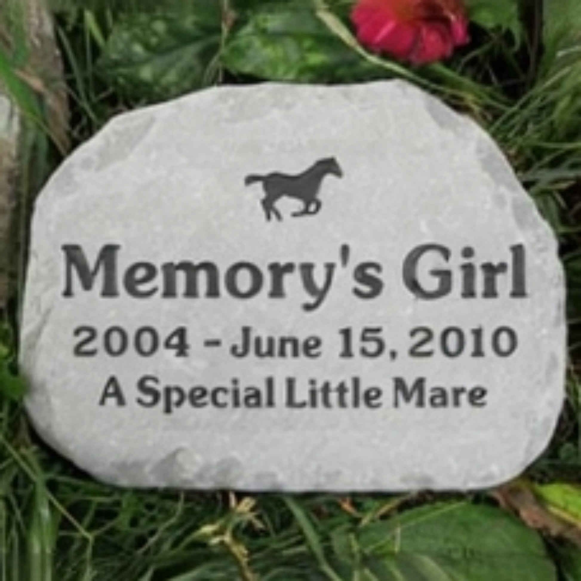 A personalized horse memorial stone engraved with the name 'Memory's Girl', dates '2004 - June 15, 2010', and the phrase 'A Special Little Mare' with a small horse silhouette, placed outdoors in grass among green leaves.