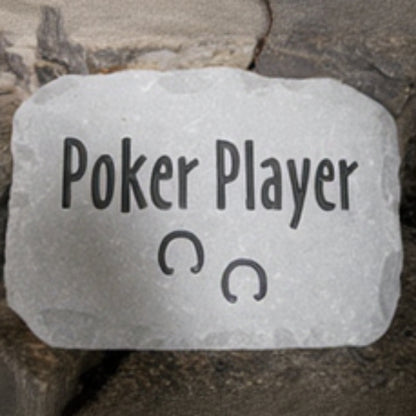 A rectangular gray stone plaque engraved with the words 'Poker Player' and two horse shoe symbols, set against a background of dark natural rocks.
