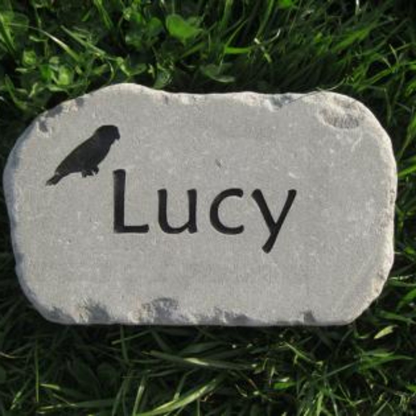 A personalized gray stone bird memorial garden marker engraved with the name 'Lucy' and a small bird silhouette, placed on green grass.