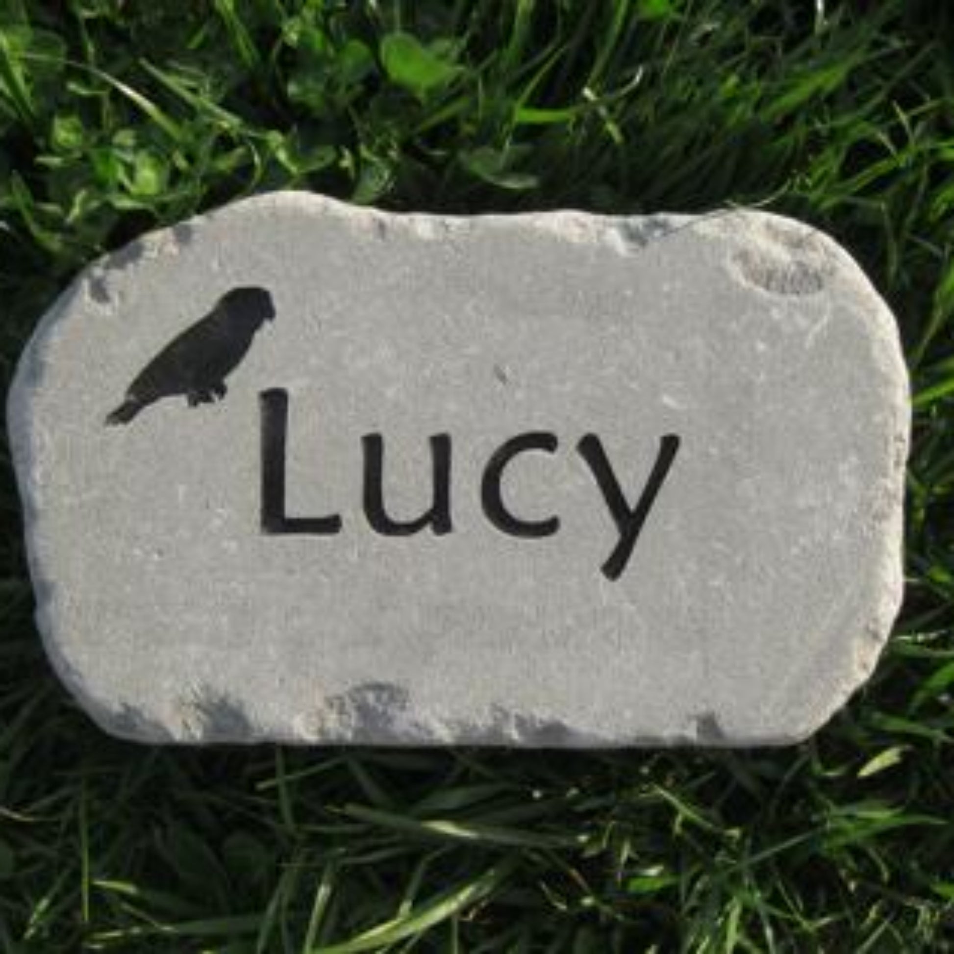 A personalized gray stone bird memorial garden marker engraved with the name 'Lucy' and a small bird silhouette, placed on green grass.
