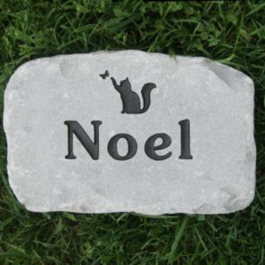 A personalized light gray stone grave marker engraved with a black cat silhouette and the name 'Noel', placed on green grass.