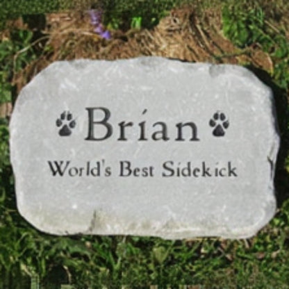 A personalized pet grave stone engraved with the name 'Brian' and the phrase 'World's Best Sidekick' with paw prints, placed on grass.